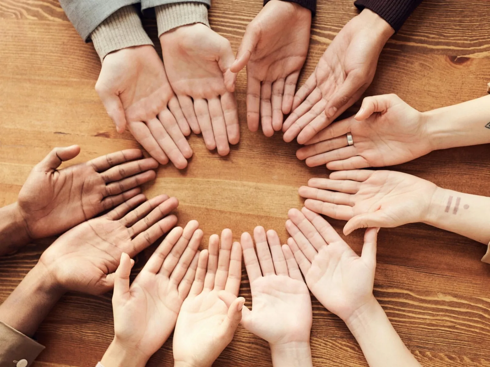 Open hands of a group of people forming a circle on a wooden table.