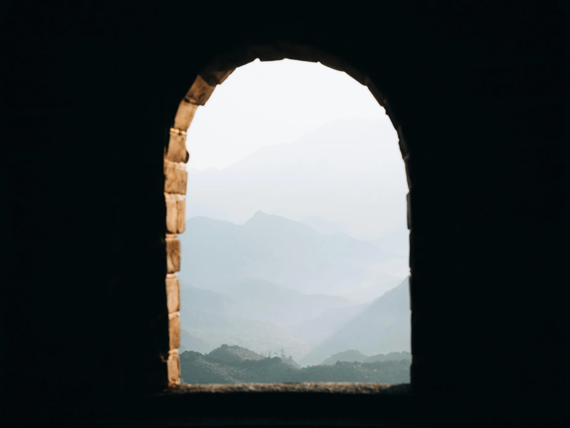 Misty mountain ridges seen through an arched window in a stone wall.